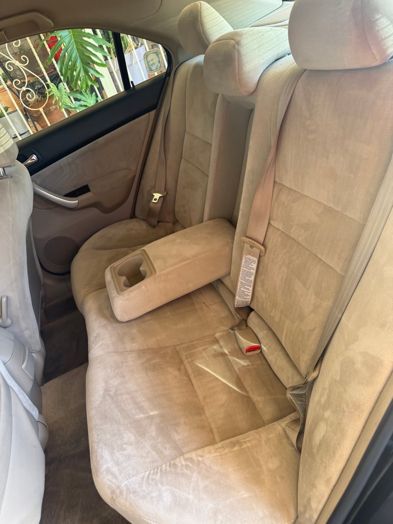 Interior view of car rear seat with tan leather upholstery, armrest, and window showing exterior