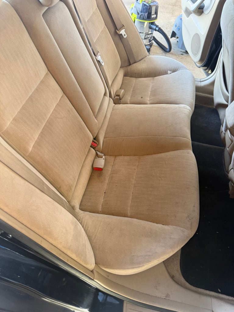 Interior view of a cars rear seats with beige or tan upholstery, showing clean fabric seating area