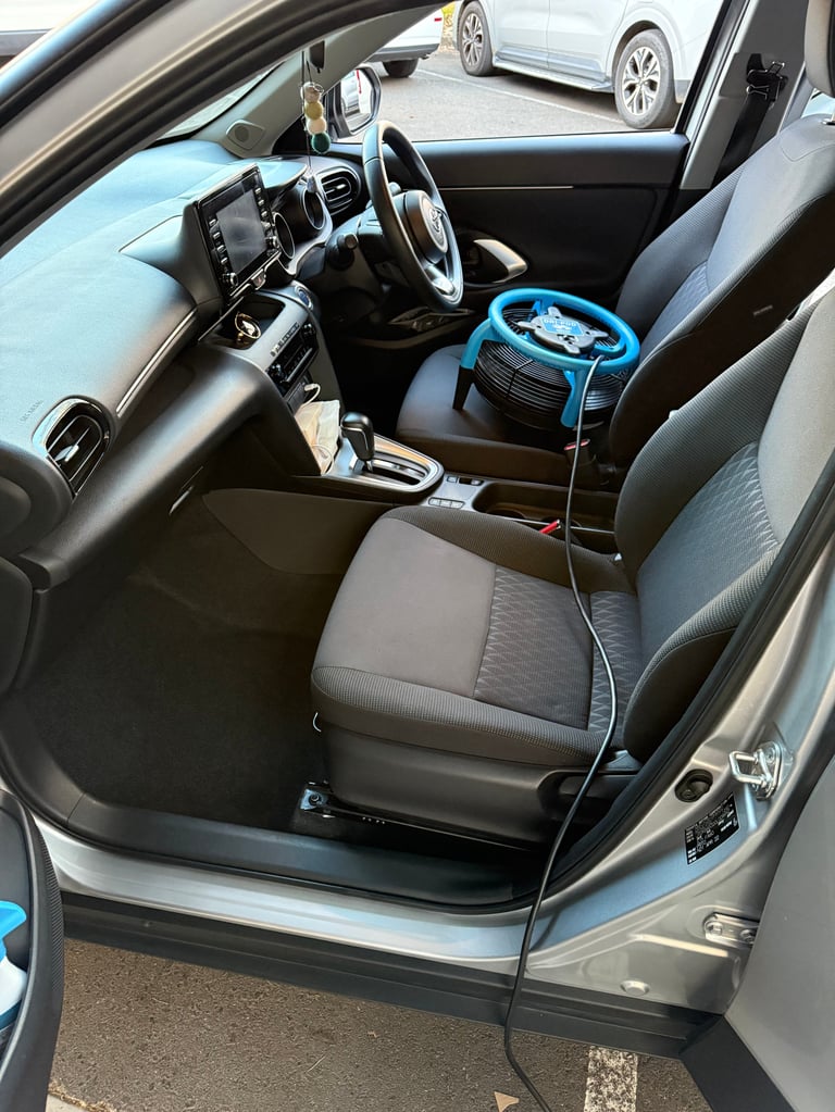 Car interior with gray seats, steering wheel, and blue portable steering wheel lock device on passenger seat