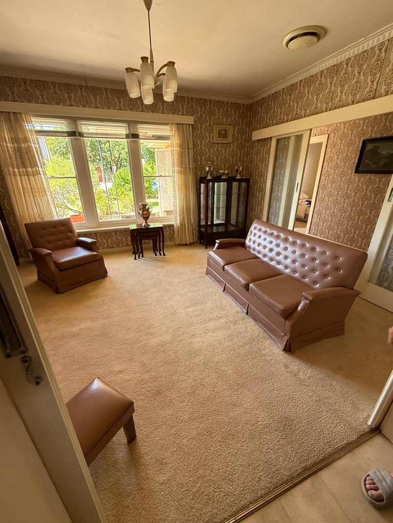 Retro living room with brown leather furniture, patterned wallpaper, and large windows overlooking trees