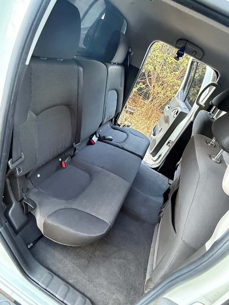 Interior view of a vehicles rear seat with gray upholstery and visible window showing outdoor trees