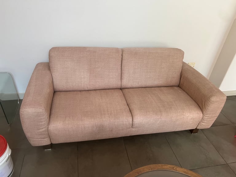 Beige upholstered two-seater sofa with rounded armrests and cushioned seating on a dark hardwood floor