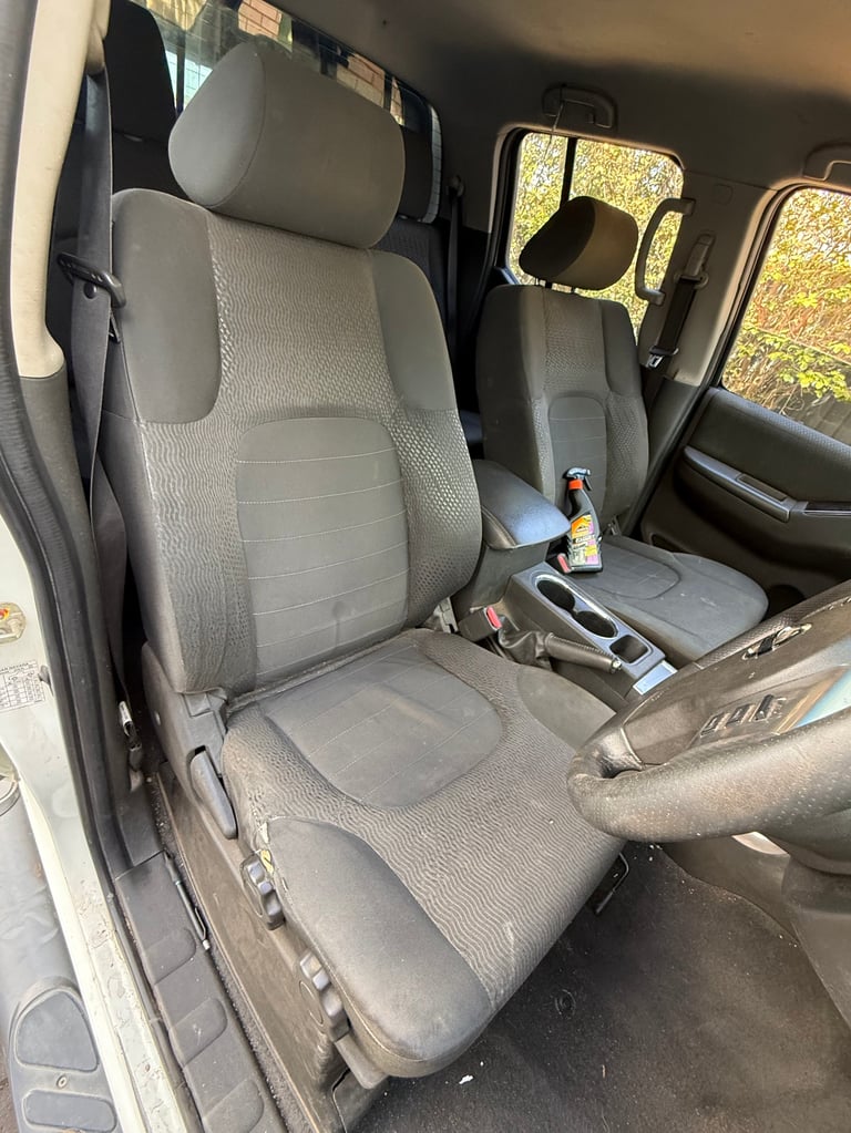 Interior view of a vehicle cabin showing gray fabric seats with a small bottle on the center console and windows with autumn foliage visible outside