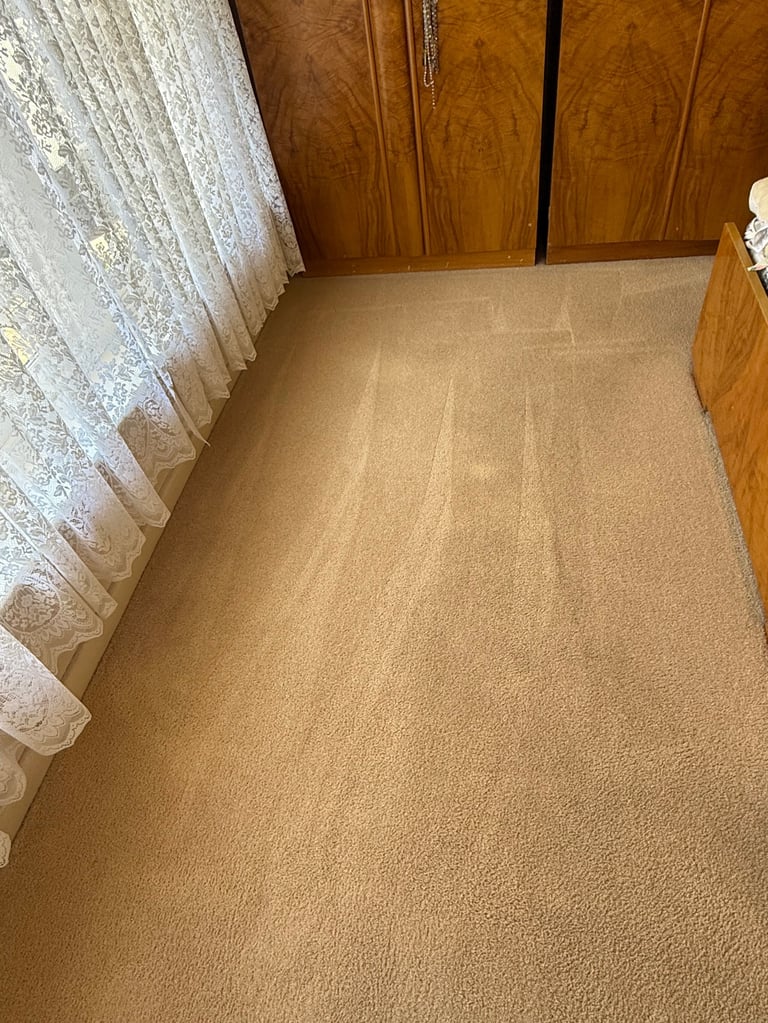 Tan carpet in bedroom with wooden furniture and lace curtains on left side