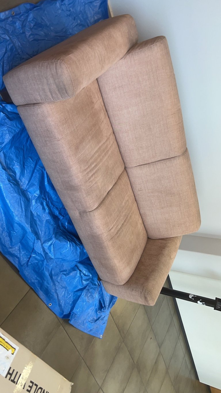 Beige upholstered armchair wrapped in blue plastic sheeting, viewed from above on a tile floor